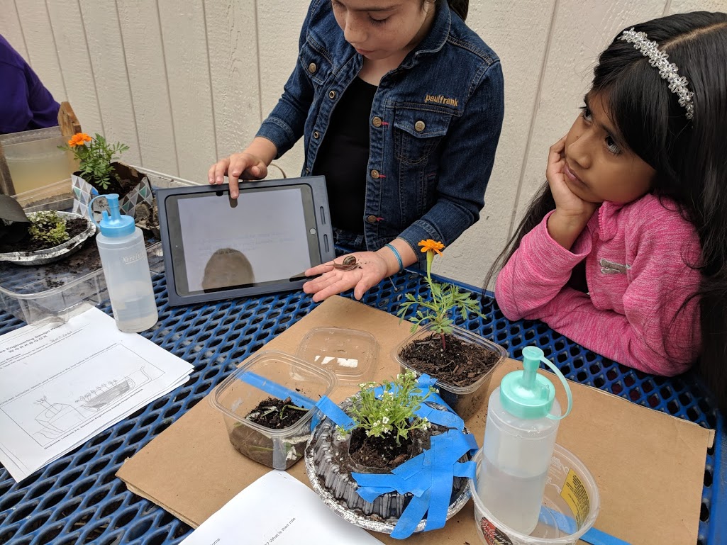 Two young female students display their biomes and presentation on an ipad