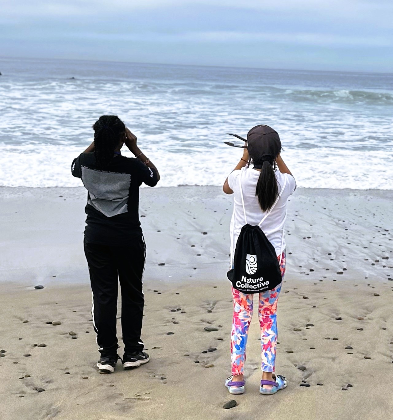 Two students looking through binoculars at the ocean for birds